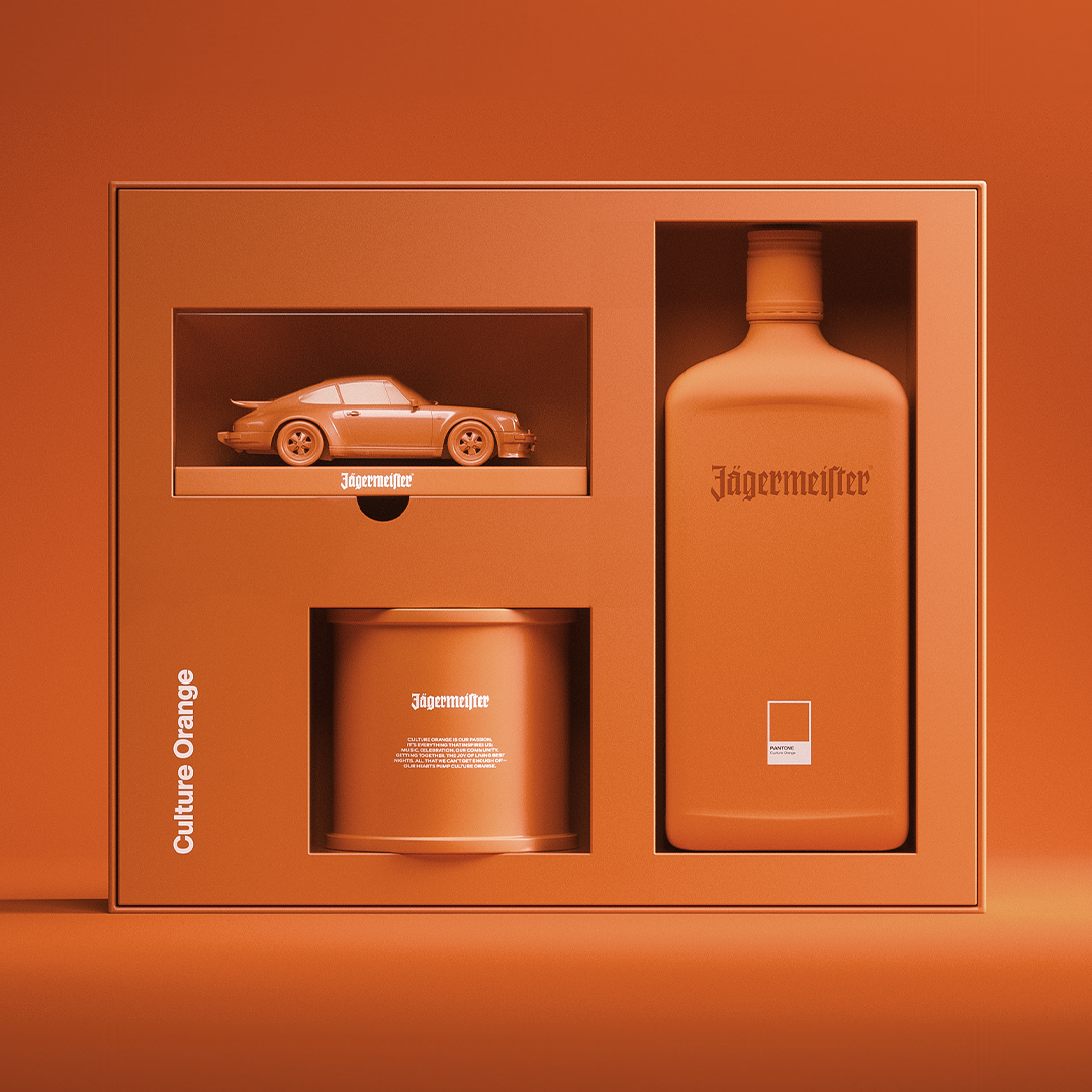 A Jägermeister 'Culture Orange' gift set in a matching orange box, featuring a miniature orange sports car, a large orange bottle, and an orange cylindrical tin, all arranged on a solid orange background.