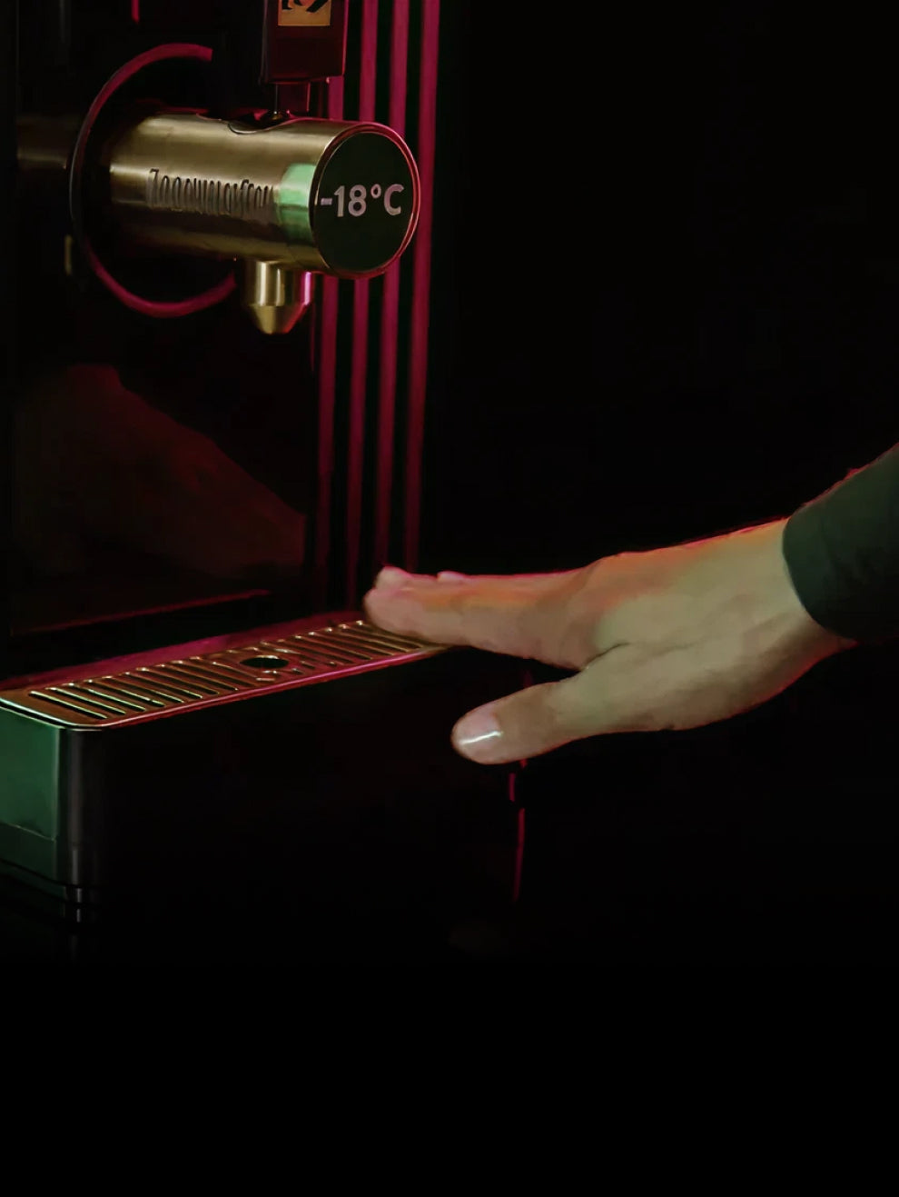 A hand pushes in a drip tray to a dark green Jägermeister dispenser, which has a thermometer showing -18°C.
